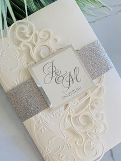 the wedding card is decorated with silver glitters and a monogrammed name tag