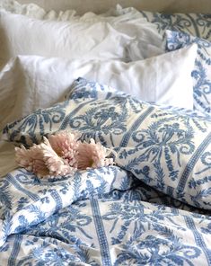 a bed with blue and white sheets, pillows and flowers