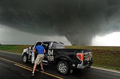 a man standing next to a black truck under a storm cloud