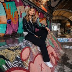 a woman sitting on top of a graffiti covered wall