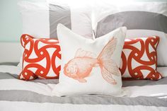 two orange and white pillows sitting on top of a bed next to an orange fish pillow