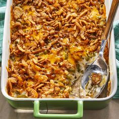 a casserole dish with chicken and cheese in it on a wooden table next to a spoon