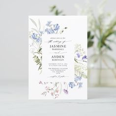 a wedding card with blue flowers and greenery on the front is displayed next to a vase filled with baby's breath