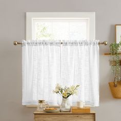 a white curtain hanging over a window next to a table with vases and flowers on it