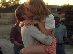 a man kissing a woman on the cheek in front of other men and women standing around