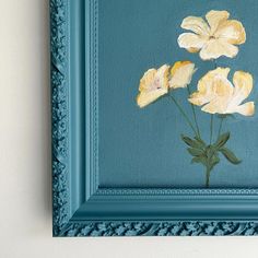 three yellow flowers in a blue frame on a white wall, with green trim around the edges