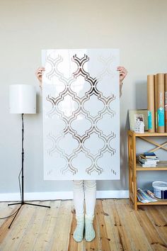 a woman holding up a large white poster in front of her face with an intricate pattern on it