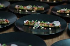 several black plates filled with food on top of a wooden table next to each other