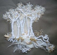 an embroidered piece with white and gold details on a gray background, including branches and flowers