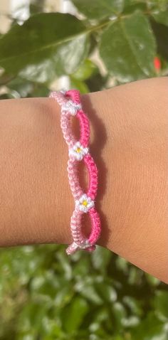 a pink and white bracelet on someone's arm with green leaves in the background