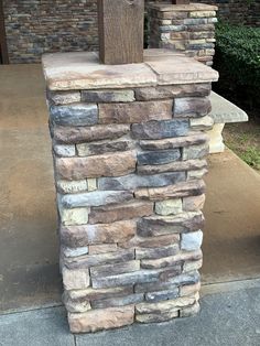 a stone pillar sitting on the side of a sidewalk next to a tree and bushes