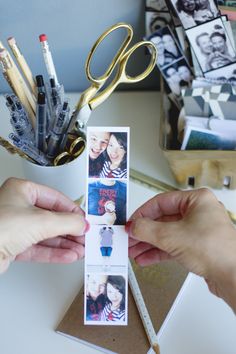 two hands holding an open photo book with photos on it and scissors in the background