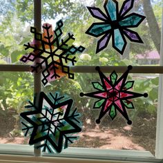 three paper snowflakes hanging on a window sill in front of some trees