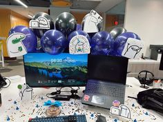 a laptop computer sitting on top of a desk next to a keyboard and mouse with balloons in the background