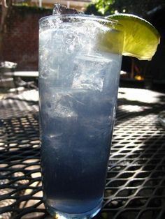 a tall glass filled with ice and a lemon wedge on top of a metal table