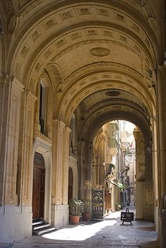 an archway in the middle of a building with potted plants on either side and a bench at the end