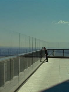 a man standing on top of a glass walkway next to the ocean in front of him