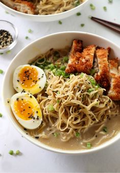 two bowls filled with ramen and topped with fried eggs, scallops, and green onions