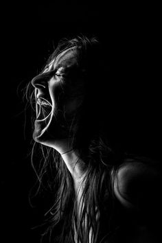 black and white photograph of a woman with her mouth wide open in the dark, screaming