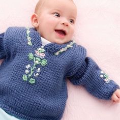 a baby laying on top of a pink blanket wearing a blue knitted sweater with flowers