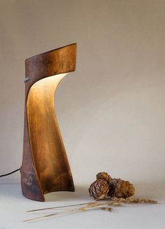 a wooden table lamp sitting on top of a white surface next to some dried up pine cones