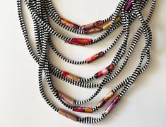 Embrace summer with a statement cord necklace that's anything but ordinary. This unique, multi-stranded textile yarn necklace is crafted from a delightful blend of soft, lightweight cotton and hand-painted beads. It's a layered masterpiece bursting with vibrant stripes and pops of color from red - purple - gold beads. It's the perfect summer accessory, adding instant sophistication to a simple t-shirt and jeans or elevating a flowy blouse.  This long fabric necklace combines a range of lengths from 7.8 to 15.7 inches, ensuring a comfortable fit that flatters any outfit. More than just a necklace, it's a piece of wearable art, a true conversation starter. Complete your bohemian or summer look, ditch the mass-produced jewelry and embrace the unique - this handcrafted scarf necklace  is a tru Multi-strand Black Necklace For Beach, Black Multi-strand Necklace For Beach, Tshirt Necklace, Yarn Necklace, Bohemian Scarves, Painted Beads, Hand Painted Beads, Black And White Scarf, Burning Man Outfits