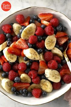 a white bowl filled with sliced bananas, raspberries and blueberries next to a spoon