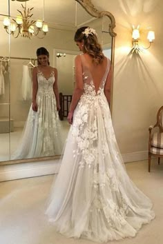 a woman in a wedding dress looking at herself in the mirror with her back to the camera