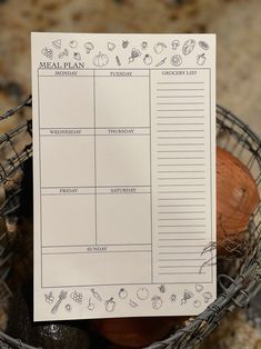 a meal planner sitting on top of a basket filled with fruit and vegetables, next to an eggplant