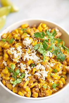 a white bowl filled with corn and topped with feta cheese, cilantro and parsley