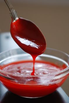 a spoon is pouring red liquid into a glass bowl on a black countertop,