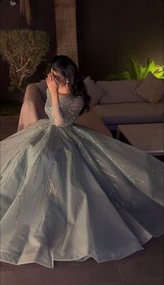 a woman in a ball gown is sitting on the floor with her hands to her face