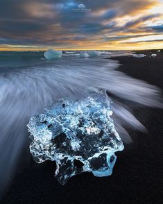 an iceberg floating on top of a black beach next to the ocean