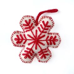 a red and white snowflake ornament hanging from a string on a white surface