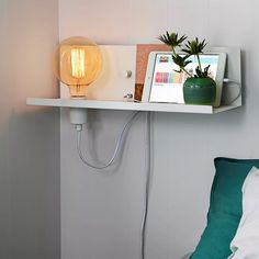 there is a light that is on the shelf above the bed and next to it is a plant