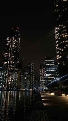 the city skyline is lit up at night with lights reflecting in the water and skyscrapers