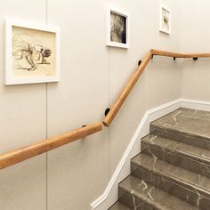 some pictures are hanging on the wall next to a set of stairs with wooden handrails