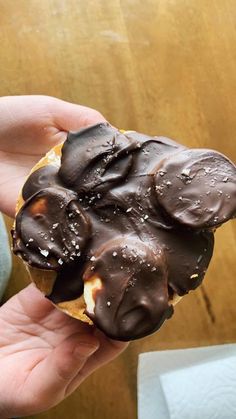 a person holding a chocolate covered doughnut in their hand