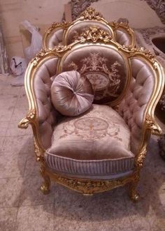 an ornate gold and pink chair with pillows on it