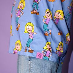 Dive into nostalgia with our vibrant and fun Disney’s Lizzie McGuire AOP. This unisex tee features an all-over print pattern of everyone's favorite animated inner voice, Lizzie McGuire, against a bold purple background. Relive the iconic moments and memorable expressions of Lizzie Mcquire as she navigates through the adventures of adolescence. Whether you're a die-hard fan or simply seeking a touch of retro charm, our AOP guarantees to add a playful pop to your wardrobe. 100% Cotton All-over Print Pattern Unisex Fit Printed Details Disney Licensed Product Model 1 is wearing a size MediumModel 2 is wearing a size XL Purple Cartoon Print Fun T-shirt, Purple Cartoon Print Top For Streetwear, Playful Purple Tops With Cartoon Print, Purple Character Print Top For Streetwear, Purple Cotton Tops With Cartoon Print, Playful Purple T-shirt With Graphic Print, Playful Purple Graphic Print T-shirt, Purple Cotton Top With Character Print, Trendy Blue Cartoon Print Shirt