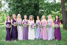 a group of women standing next to each other in purple and lavender dresses on grass