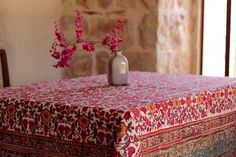 a vase with pink flowers sitting on top of a red and blue table cloth next to a stone wall