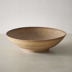 a large brown bowl sitting on top of a table next to a white wall and floor