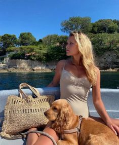 a woman sitting on the back of a boat with her dog next to her purse