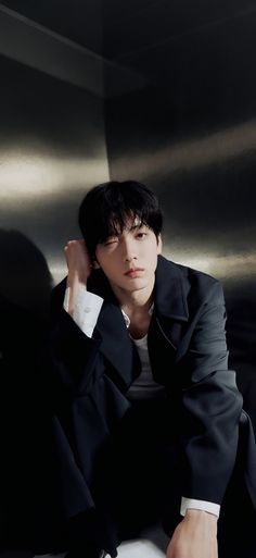 a young man sitting on top of a white chair wearing a black suit and tie