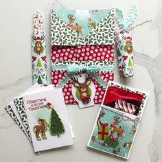 christmas cards and envelopes are laid out on a table with holiday themed wrapping paper