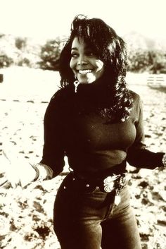 a woman standing in the sand with her hands out and smiling at the camera,