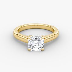 a yellow gold engagement ring with a princess cut diamond in the center, on a white background