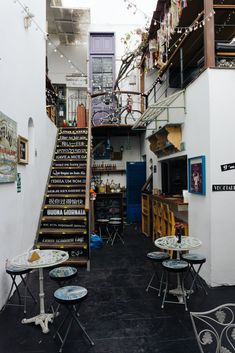 an alleyway with tables and chairs on the floor, stairs up to the second floor