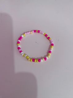 a pink, yellow and white beaded bracelet on a white surface with a shadow